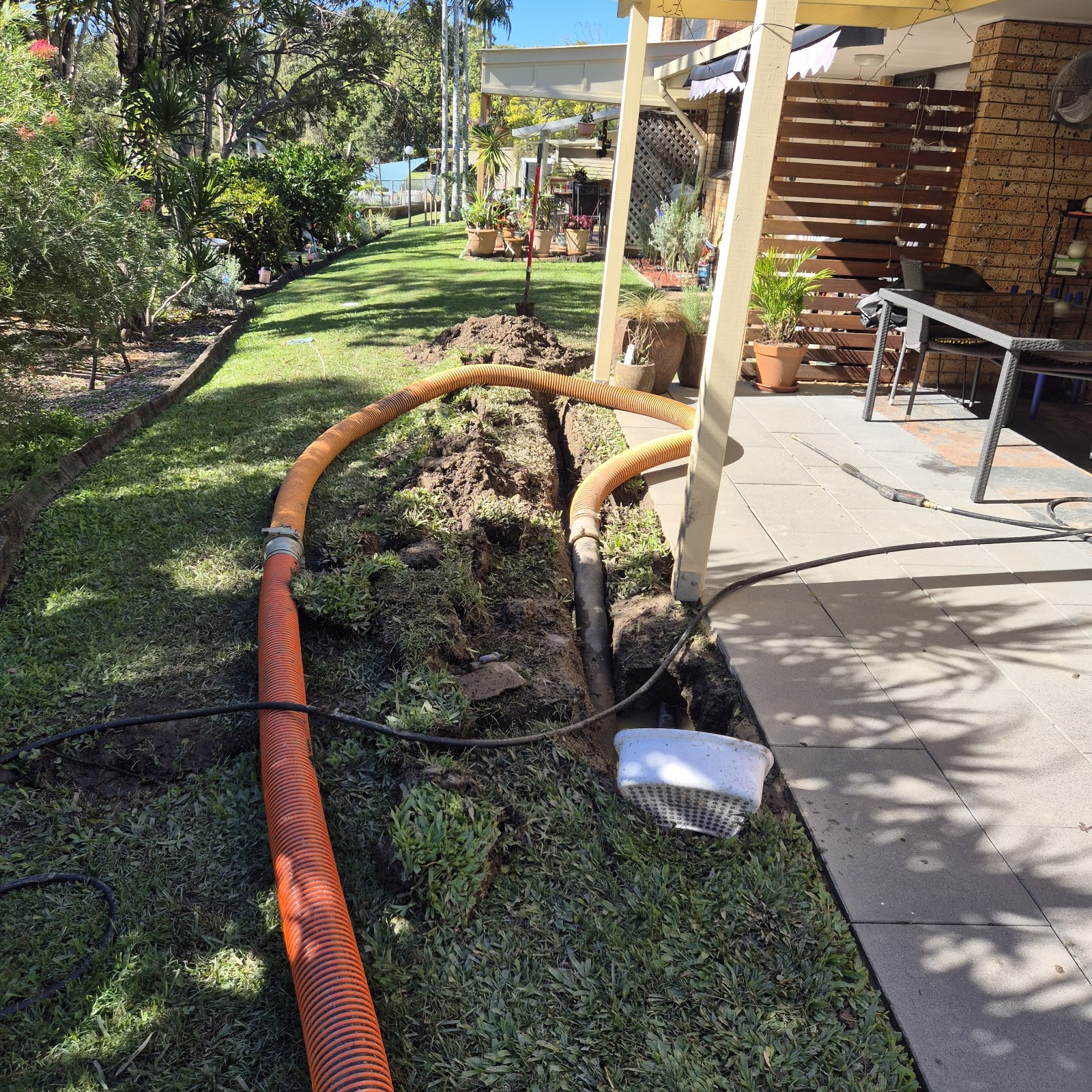 Vacuum hose in a narrow backyard trench beside a paved patio Vacuum hose in a narrow backyard trench beside a paved patio