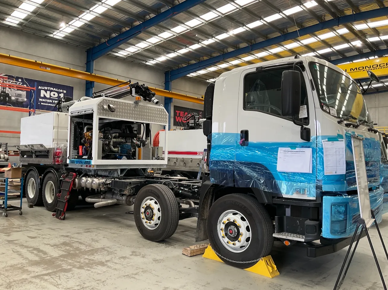 Isuzu cab with protective wrap and hydro vac equipment in the workshop Front of an Isuzu truck cab with protective wrap on the bodywork and hydro vac equipment fitted behind it in the workshop