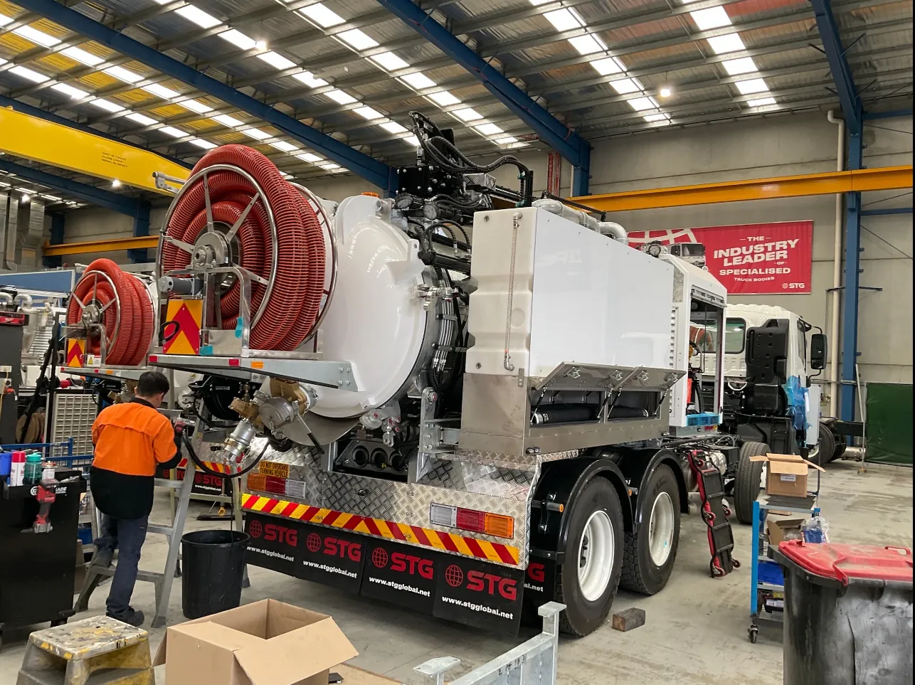Hose reel fit-out on the hydro vac truck in the workshop Workshop worker beside the rear of a hydro vac truck showing red hose reels and the vacuum tank during fit-out