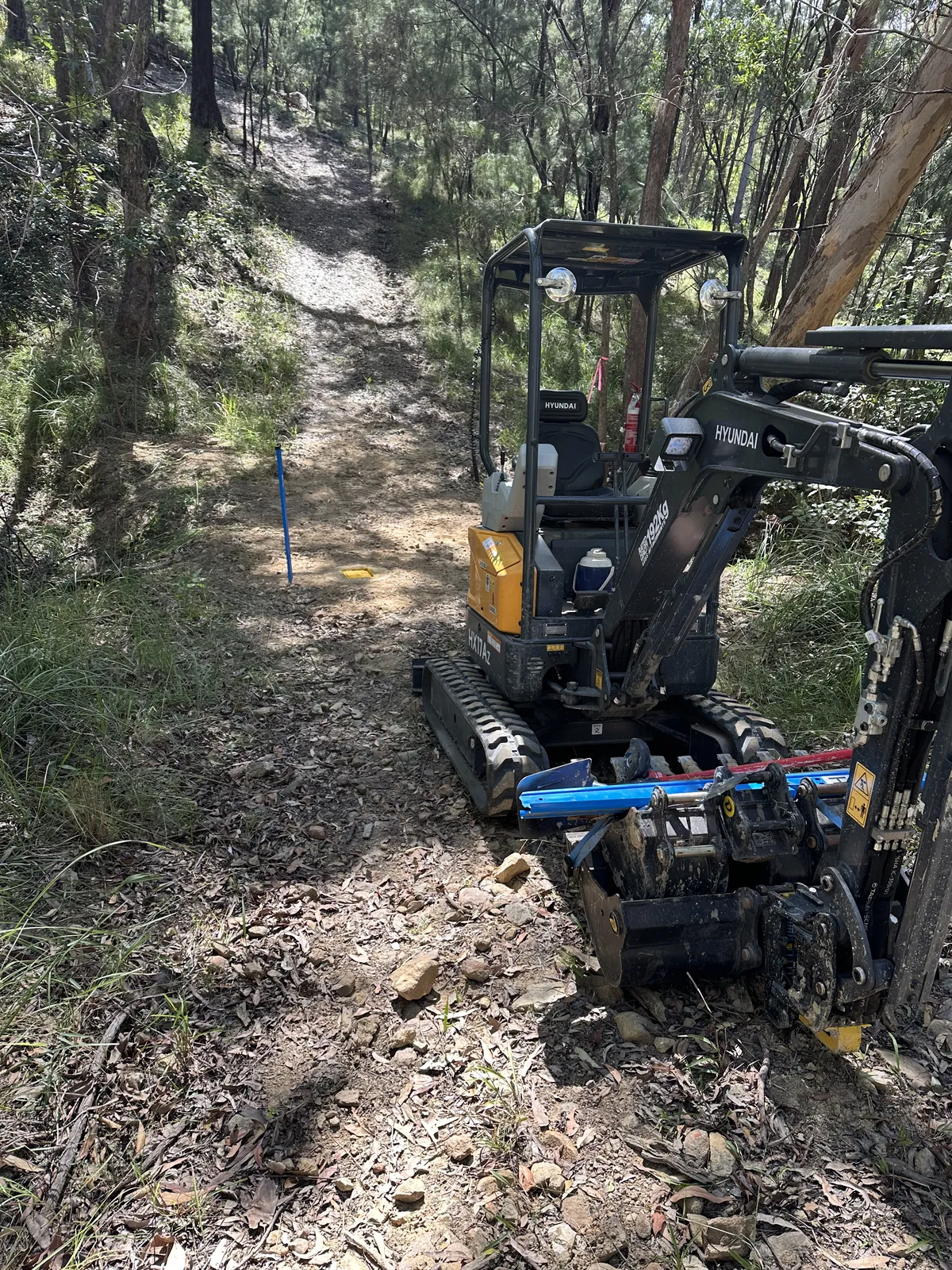Mini excavator on a bush track Hyundai mini excavator with blue conduit beside its bucket on a rocky bush track