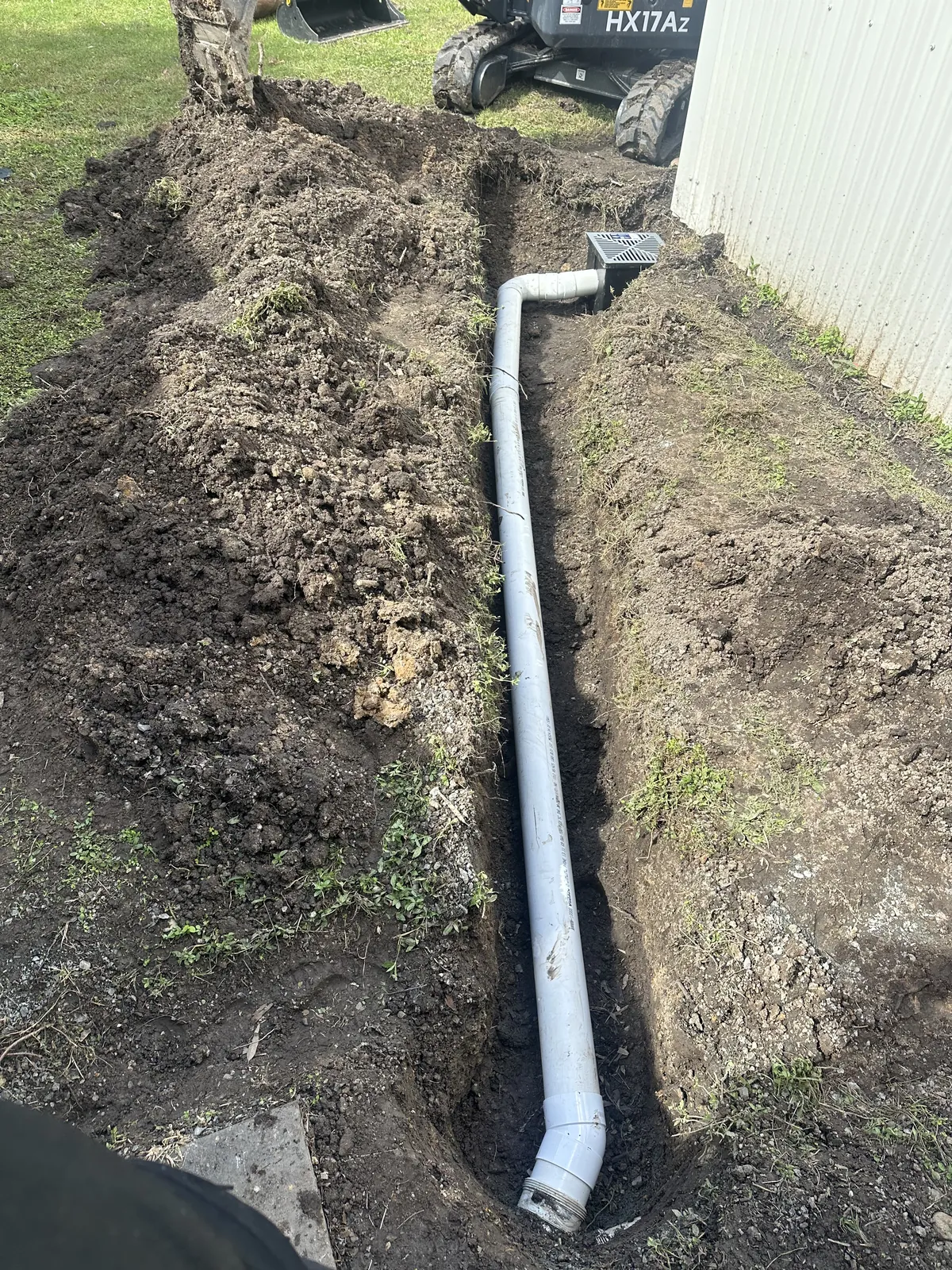 Drainage pipe and grated pit White pipe laid along an open trench leading to a grated pit beside a shed