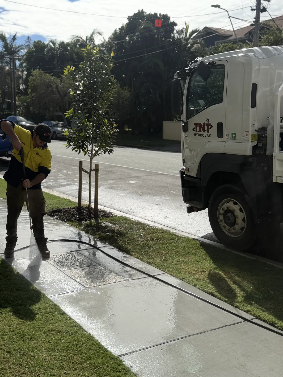 Worker holding a water lance over a wet footpath beside the white truck