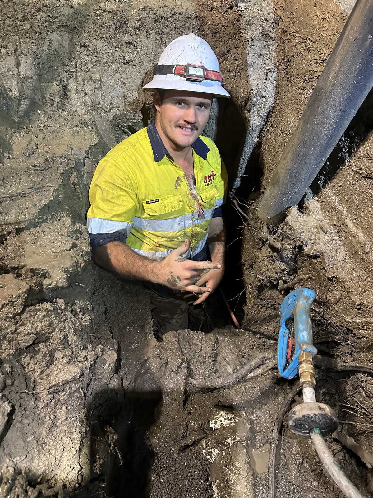 Worker in a lit excavation at night Worker in yellow high-visibility clothing in a lit excavation beside a large vacuum hose at night