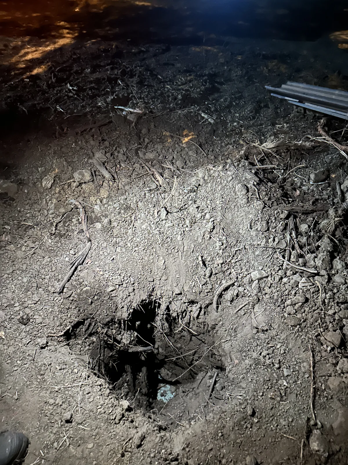 Close view of a small ground opening with exposed fittings in illuminated soil at night