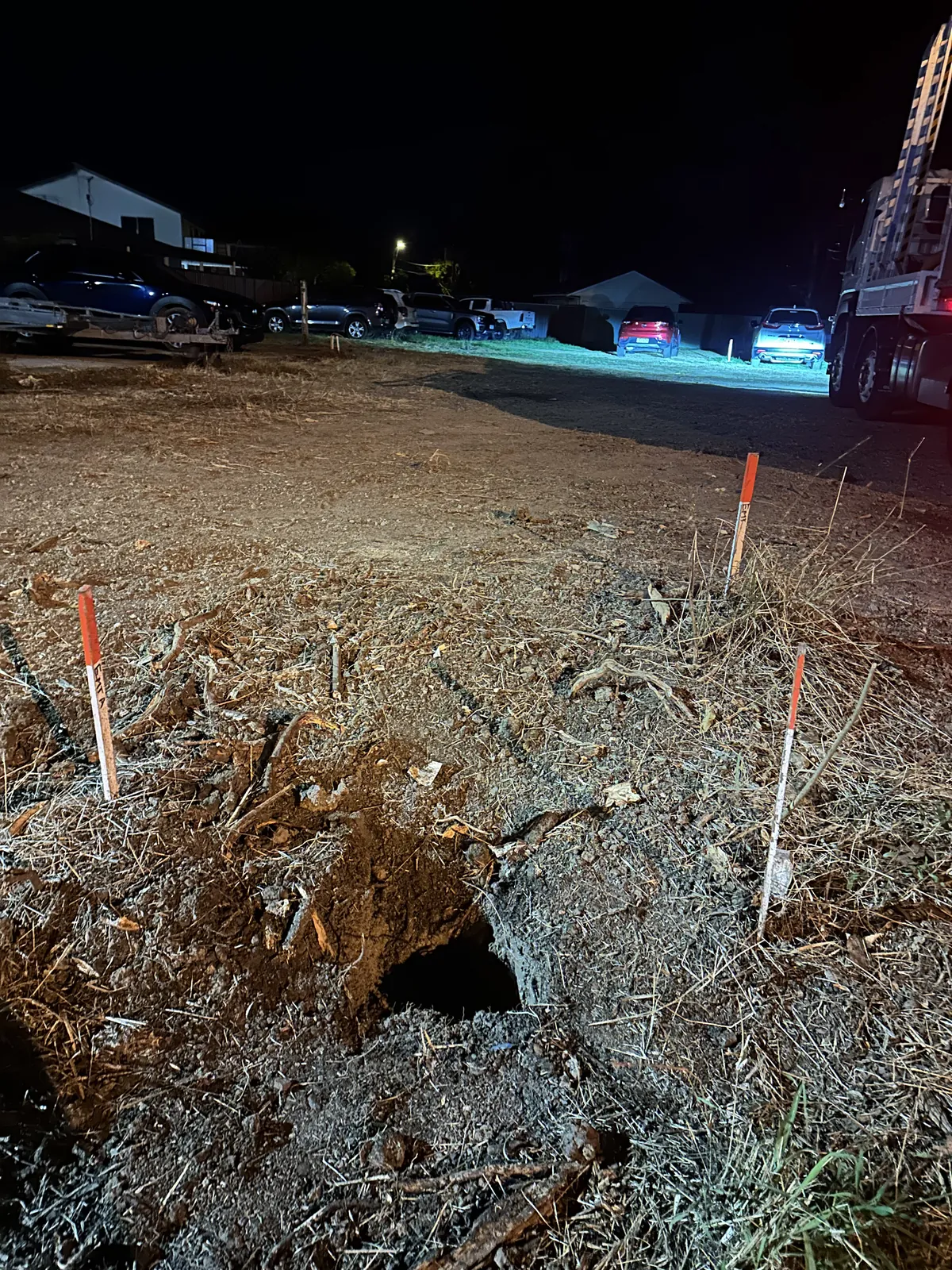 Excavated ground with upright pegs and markings beside a road under night lighting