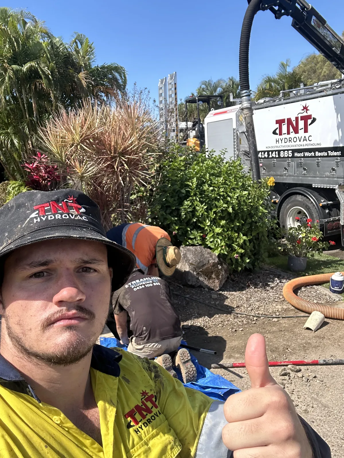 Person in high-visibility clothing giving a thumbs-up with the truck and another worker behind