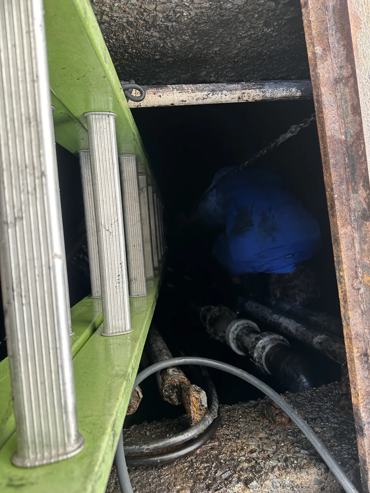 Pit with visible pipework View down into an open pit with visible pipes and hose beneath a rectangular opening beside a wall