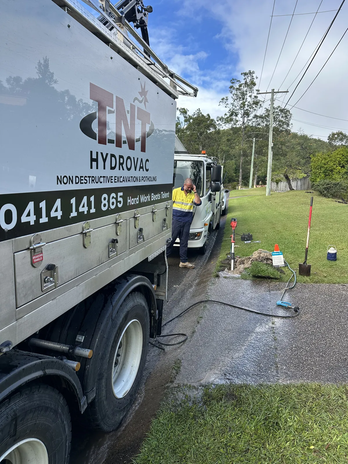 Side of the truck beside a roadside grass verge with a worker, hoses and locating equipment