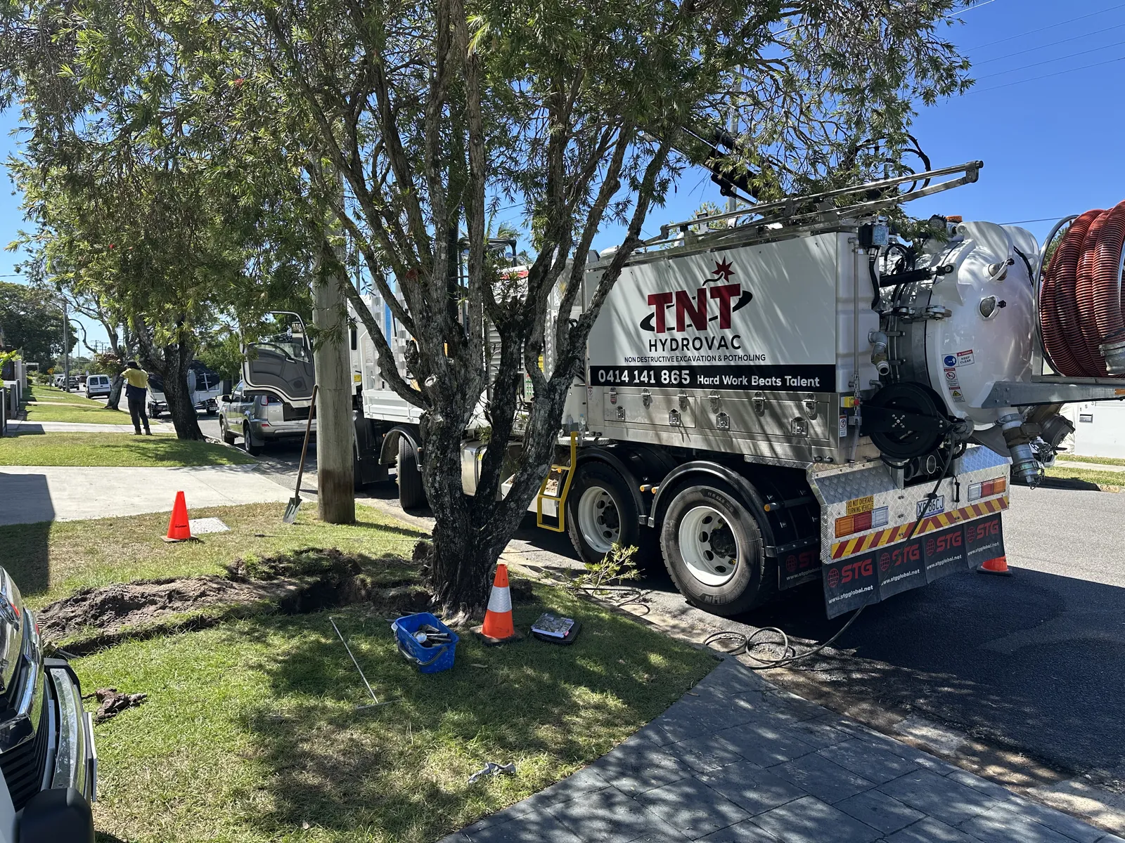 Truck beside a tree on a street verge with hoses and cones around the excavation area